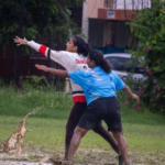 Players in a muddy field during a frisbee game, one throwing while others defend.