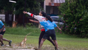 Players in a muddy field during a frisbee game, one throwing while others defend.