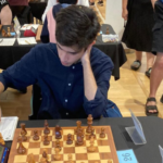 Person concentrating on a chess game, seated at a table with a chessboard and score sheet.
