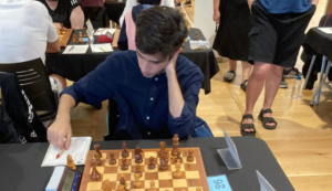 Person concentrating on a chess game, seated at a table with a chessboard and score sheet.