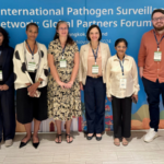 Six people standing in front of a banner for the International Pathogen Surveillance Network forum.