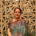 Smiling woman in a patterned sari standing in front of a geometric lattice wall
