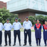 Six uniformed security personnel standing in front of a modern building with trees and signage nearby.