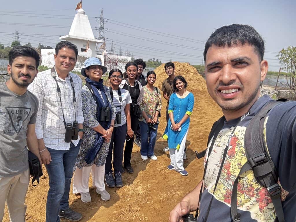 Group of people smiling outdoors on a sunny day with a temple and power lines in the background.