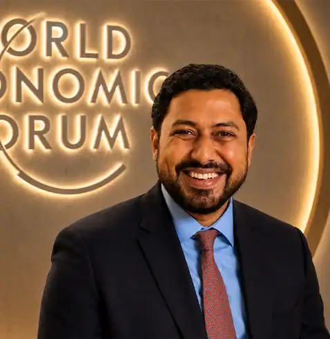 Smiling man in a suit and tie standing in front of the World Economic Forum logo.