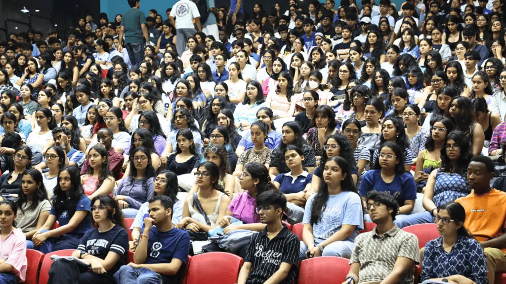 A large group of people seated in an auditorium, attentively listening and facing forward.