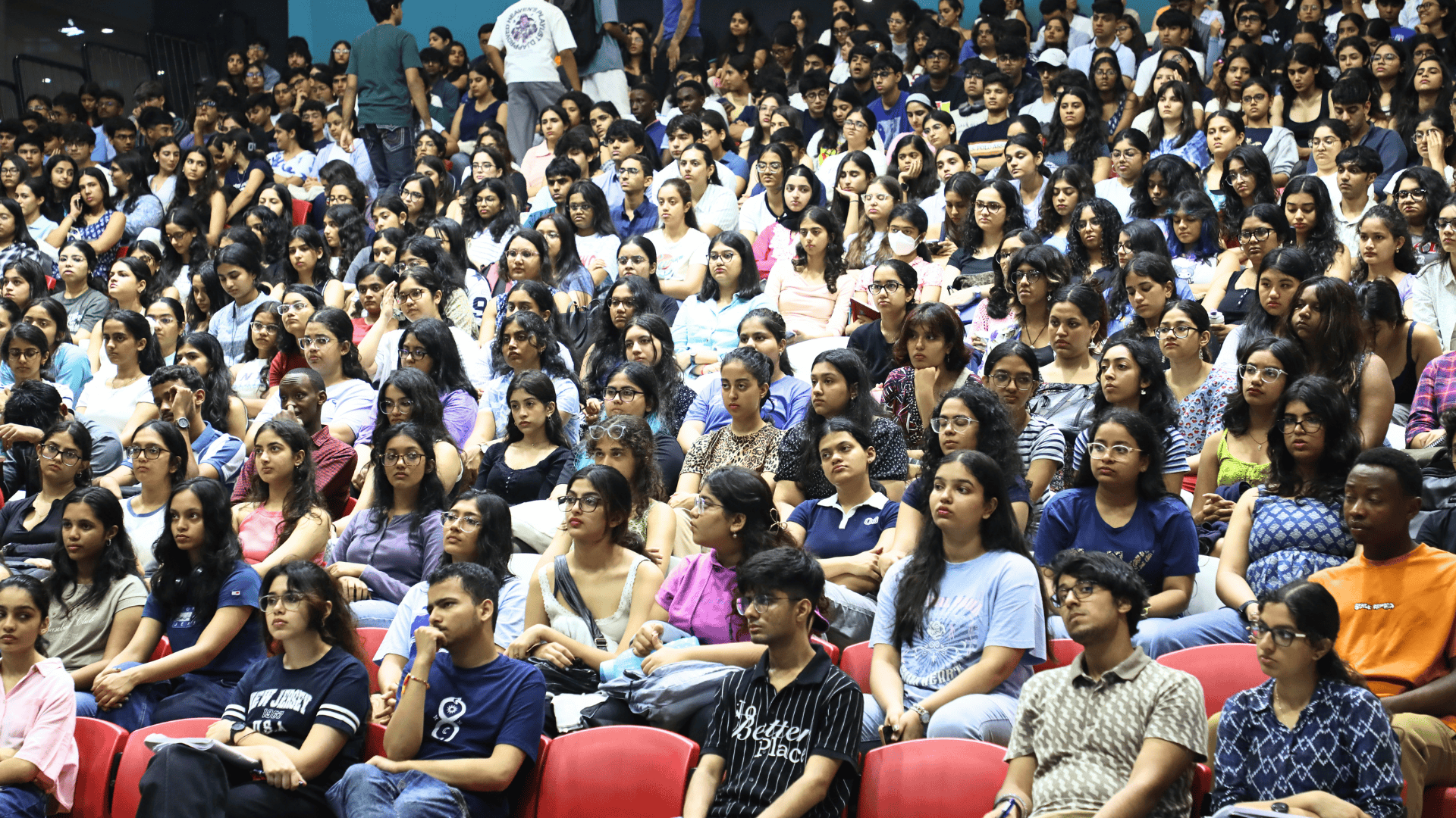 A large group of people seated in an auditorium, attentively listening and facing forward.