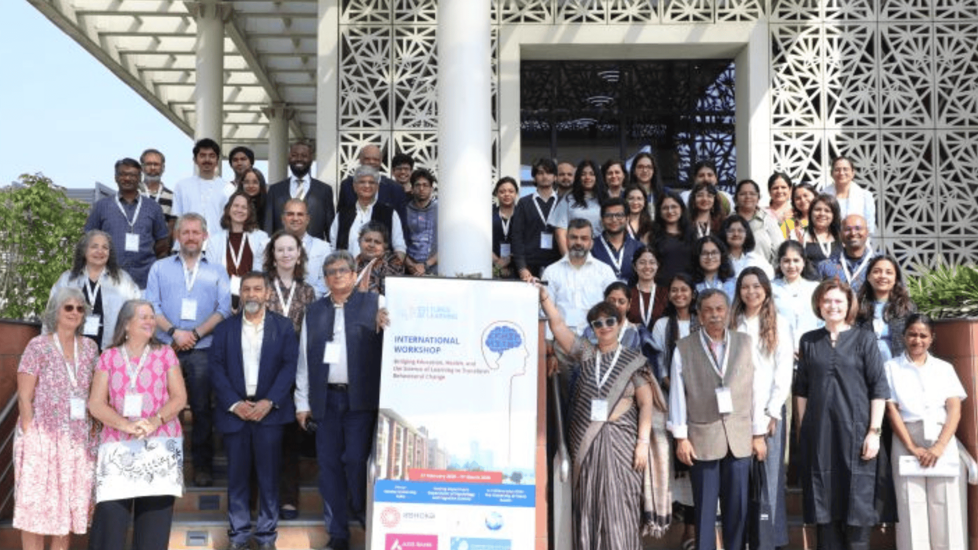 Group of diverse individuals posing on steps during an international workshop, banner in the center.