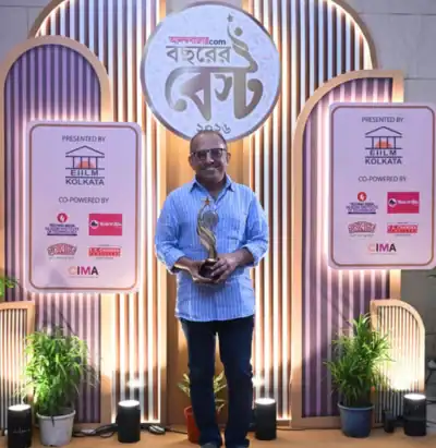 Man holding a trophy, standing between two signage boards with lights and plants in the background.