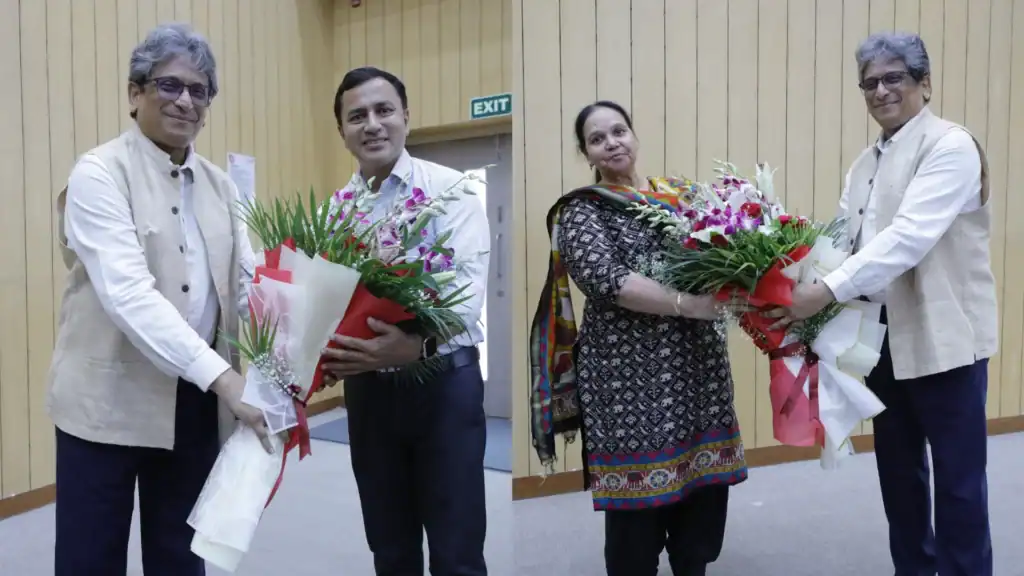 Two men and a woman exchanging bouquets in a wooden-paneled room, smiling warmly.