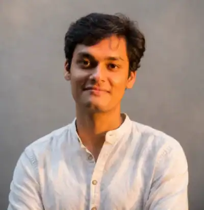 Smiling man with short dark hair wearing a white button-up shirt against a neutral background.