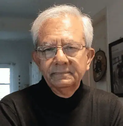 Elderly man with glasses and white hair, wearing a black turtleneck, indoors with soft lighting.